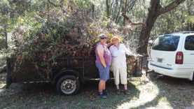 Dore and Kate posing in front of their handiwork. A trailer hitched to a station wagon is piled high with branches and vines