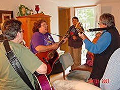 All are standing in Laurie’s living room, each holding a guitar
