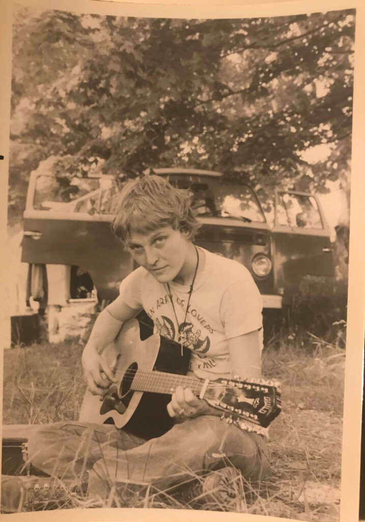 a young Falcon River in jeans and T-shirt seated on the ground playing guitar