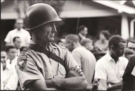 Grim Mississippi State Patrolman standing with arms crossed amid group of Black students