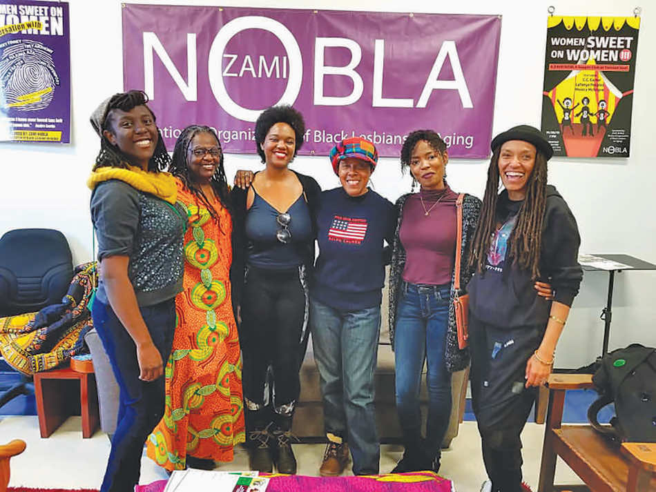 Mary Anne Adams, second from left, and five other women side hugging with zami nobla banner