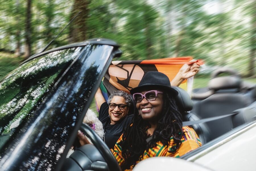 Mary Anne Adams at the wheel of top down convertible with Angela Davis in passenger seat