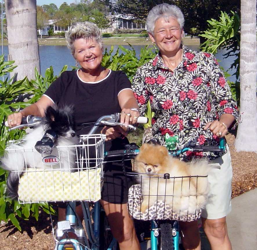Mary Gay Hutcherson and Yolanda Farnum on bicycles with little dogs in baskets on the front of their bikes