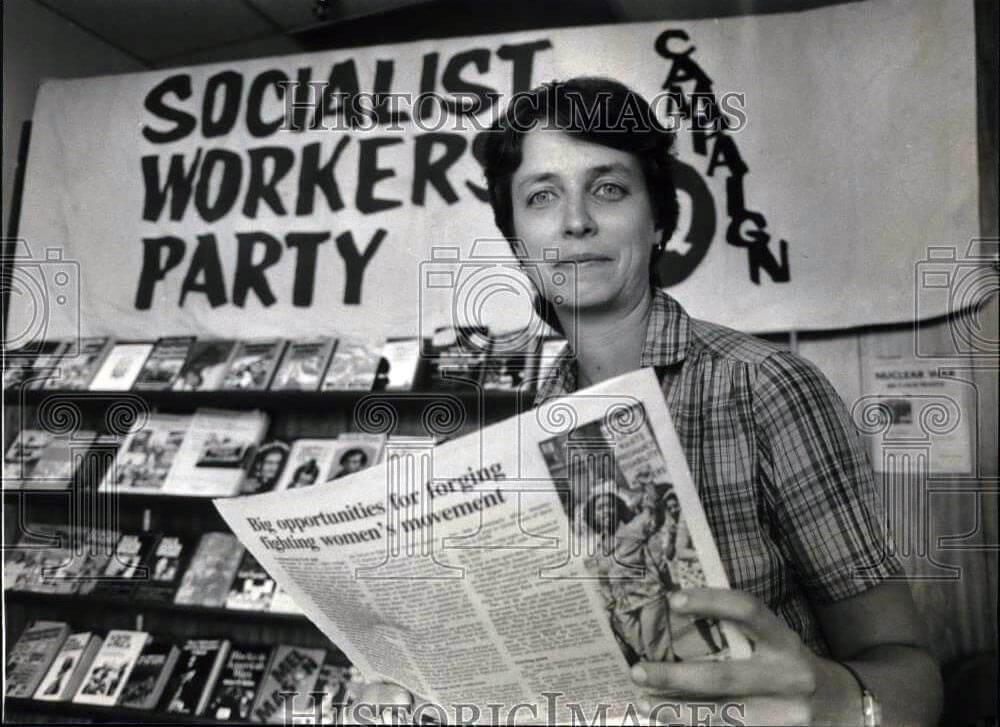 Sonja Franeta holding a newspaper and standing in front of a big Socialist Worker Party banner
