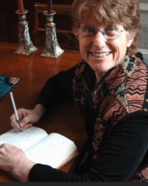 Barbara Esrig facing us while writing in an open notebook