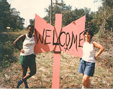 Two women standing on opposite sides of a Welcome sign in the shape of a labyrs