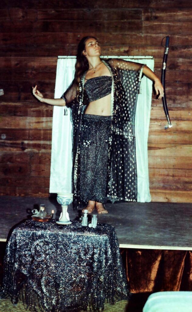 Morgana MacVicar dressed in a black two piece costume dances on stage in front of a decorated altar