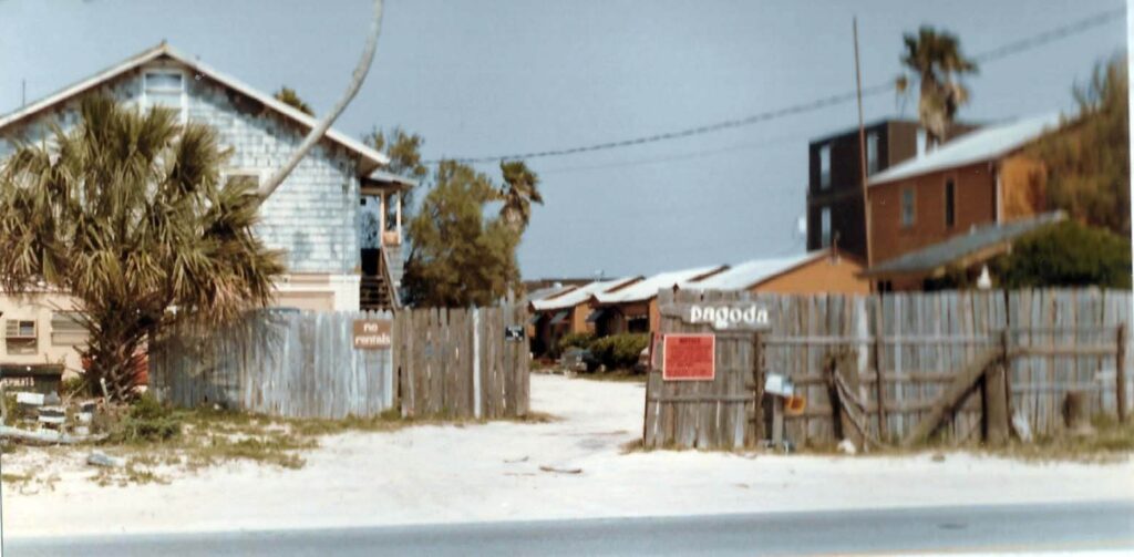A gray two story building at left and a reddish two story building at right behind a wooden fence with a Pagoda sign
