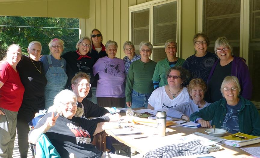 Sixteen women writers gather around a table on an porch