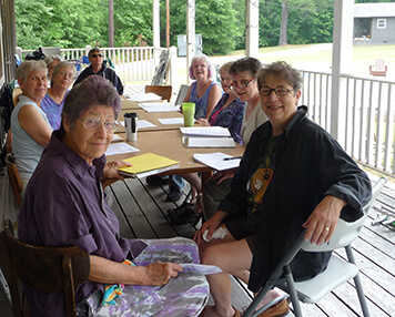 Nine women seated at a table on a porch