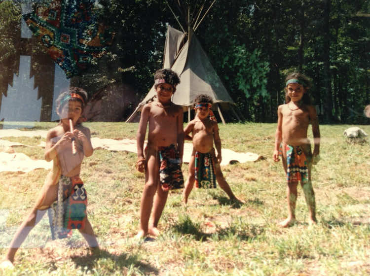 four young children dressed in native costumes in front of tepee