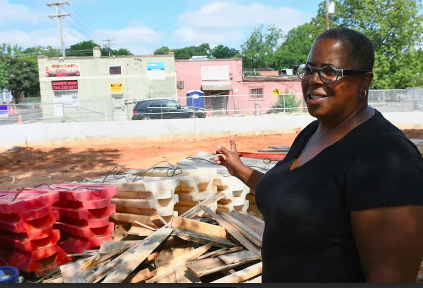 Diana Ward standing at construction site, pointing to first building purchased.