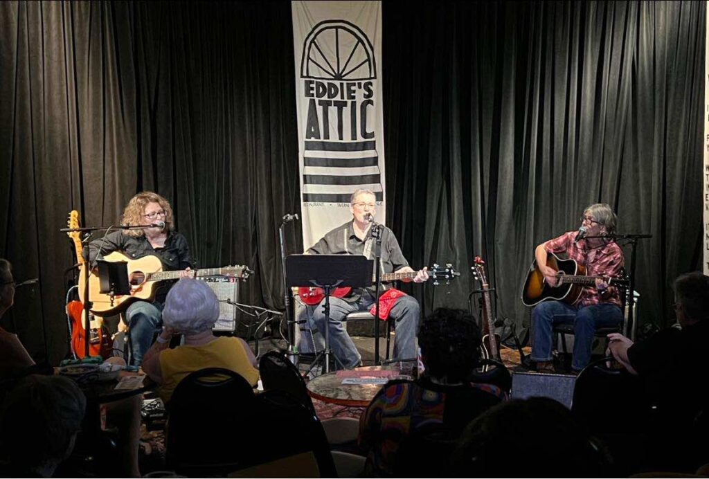 Lenny Lasater with guitar in center and guitatists Becky and Linda beside her on stage