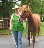 Betty Bird outdoors with a reddish brown horse She carries a white cane