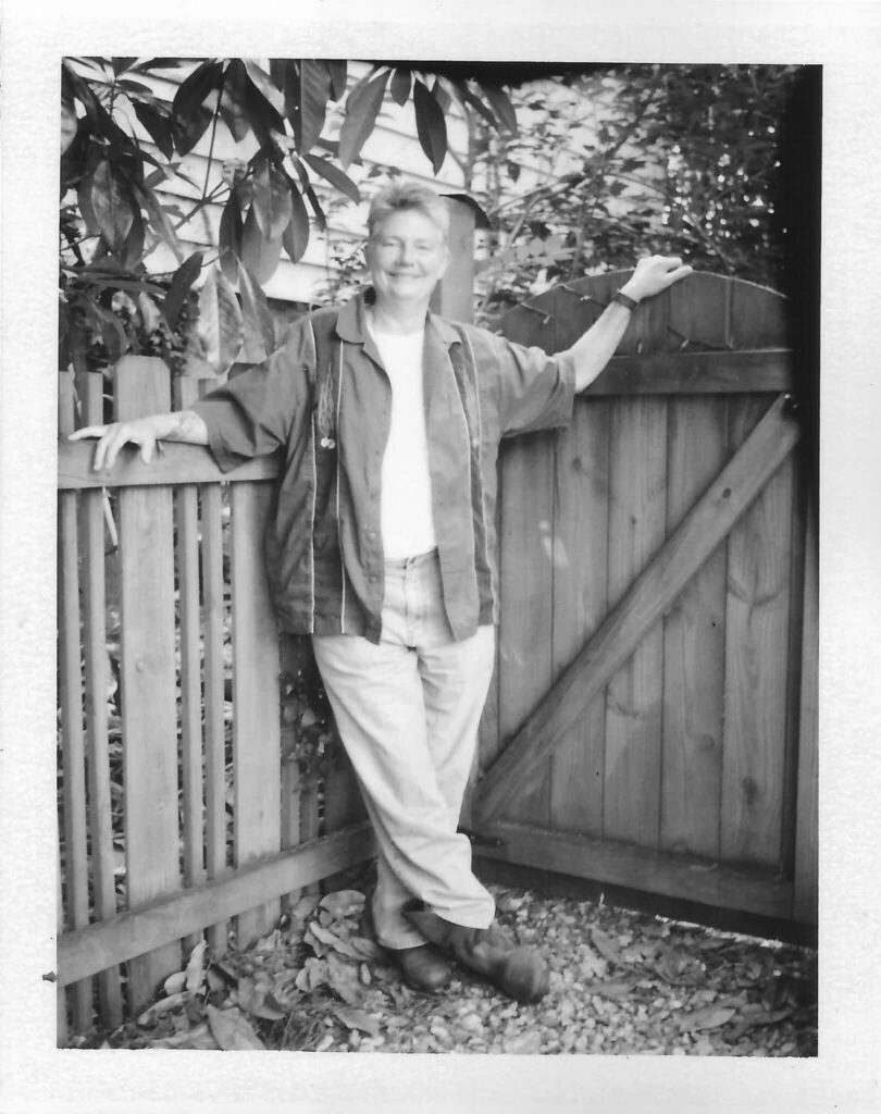 Mendy Knott, Hill Poet standing relaxed against an outside wooden gate