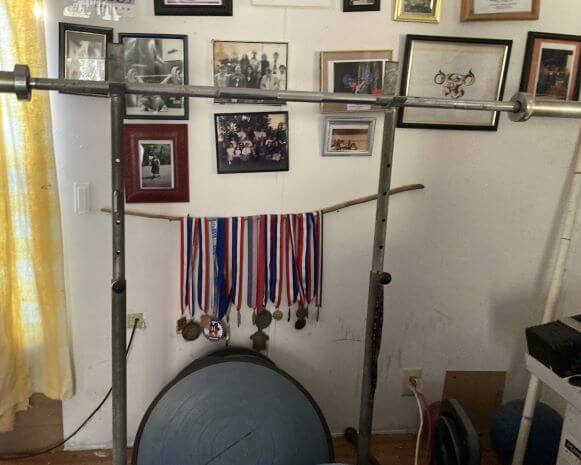 Jaen Black weightlifting bench and trophy wall with many medals and photos behind it