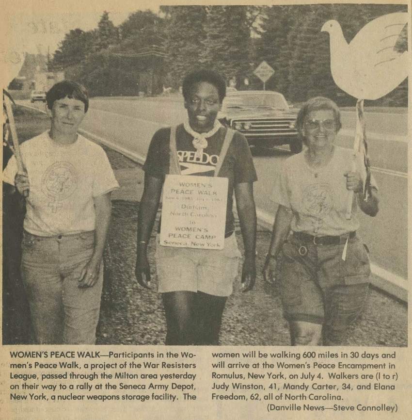 Mandy with sign around neck walking between two women