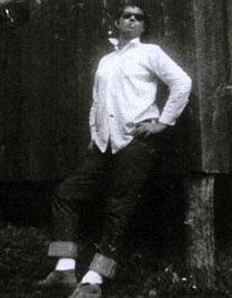 Merril Mushroom in a man's white shirt and dark glasses leaning proudly against a wall