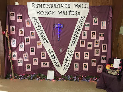 Over 30 photos mounted on a fabric backdrop surrounding a V-shaped banner reading Remembrance Wall Womonwriters Southeast Lesbian Writers Conference