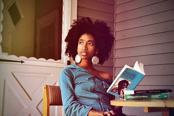 Alexis Pauline Gumbs sitting on porch holding an open book