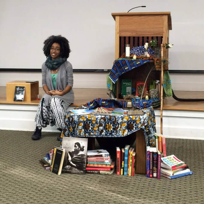 Alexis sitting on stage with altar beside her and books in crate below