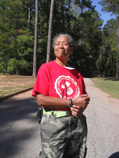 Blanche Jackson stands in a road grinning with pine trees behind her