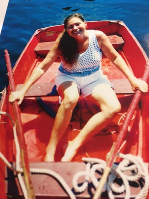 A smiling Bonnie sitting in a red rowboat holding on to oars