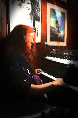 Flash Silvermoon playing double keyboard next to large poster of Janis Joplin