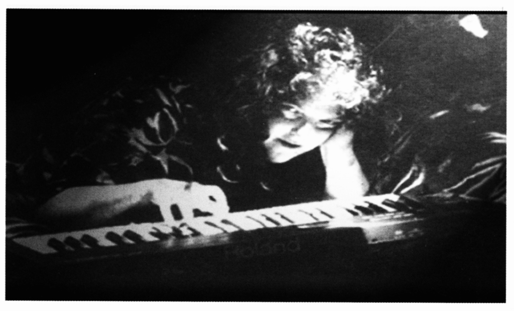 Flash Silvermoon surrounded by spooky light, playing a keyboard with her right hand, her head resting on her left hand