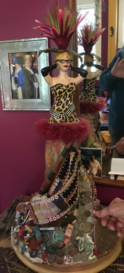 A china figurine in a leopard bathing suit with a flamboyant headpiece and a skirt swirling around the legs dotted with coins