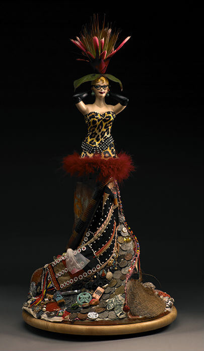 A china female figure in a leopard swimsuit with a flamboyant headdress and a swirling skirt dotted with coins all against a black background