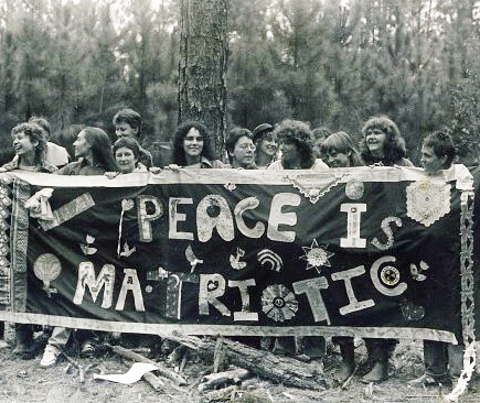 A bunch of women at a peace camp hold a large banner saying Peace is Matriotic