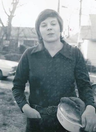 Saralyn Chesnut, young and dyky, holds casserole dish in one hand, the other posed in jeans pocket.