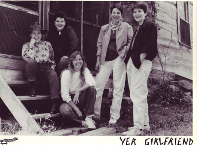 The five members of the band pose outside an old house. They are dressed casually in jeans and khakis.